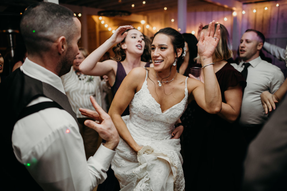 The bride and groom share a joyous dance surrounded by happy guests at their wedding reception, exemplifying the vibrant energy and fun captured by Lindsey Paradiso Photography.