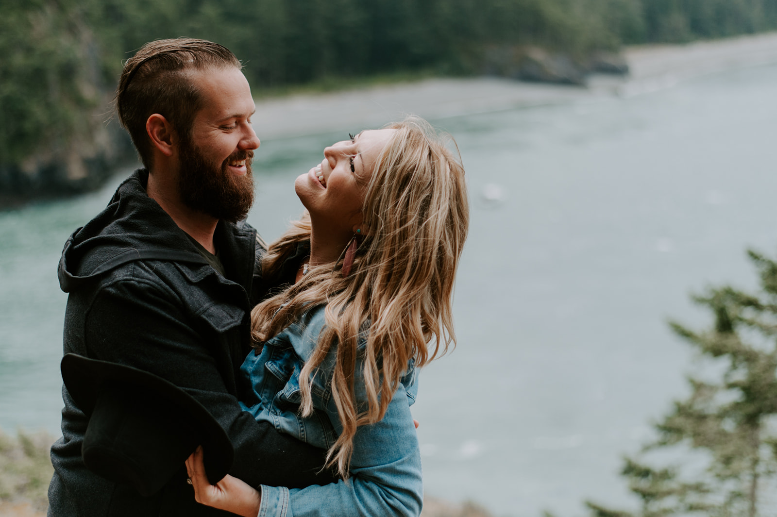 Couple laughing together, with the ocean and cliffs in the background.