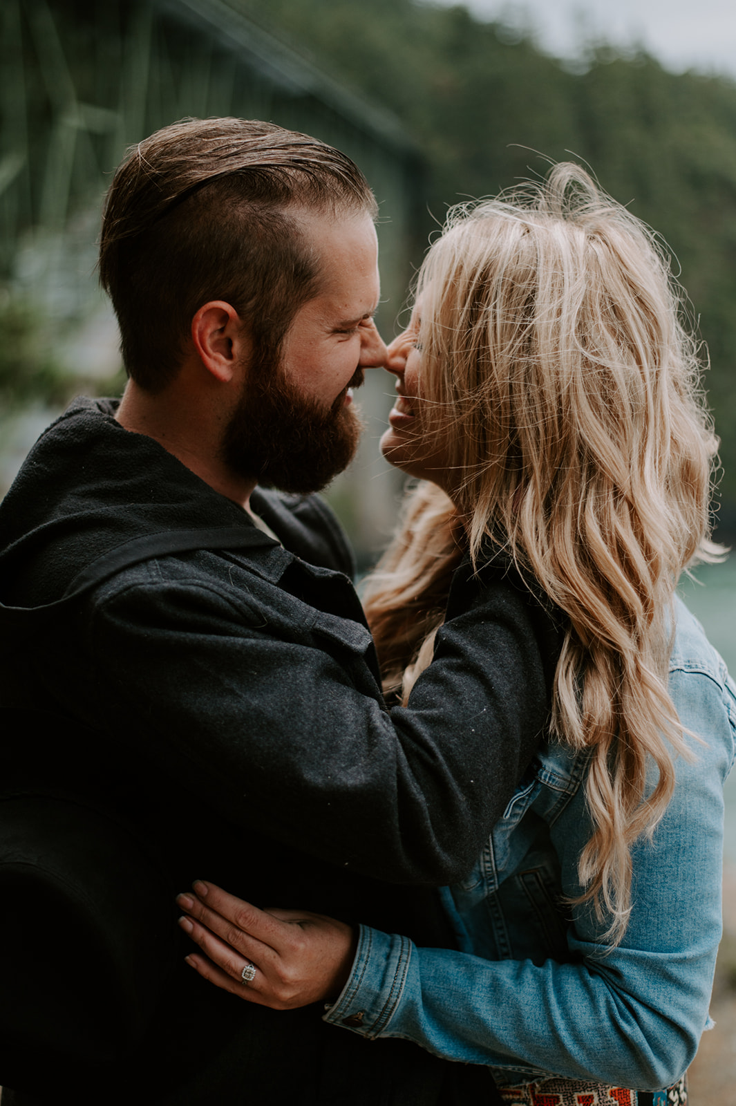 Couple standing close together, holding each other near the ocean.