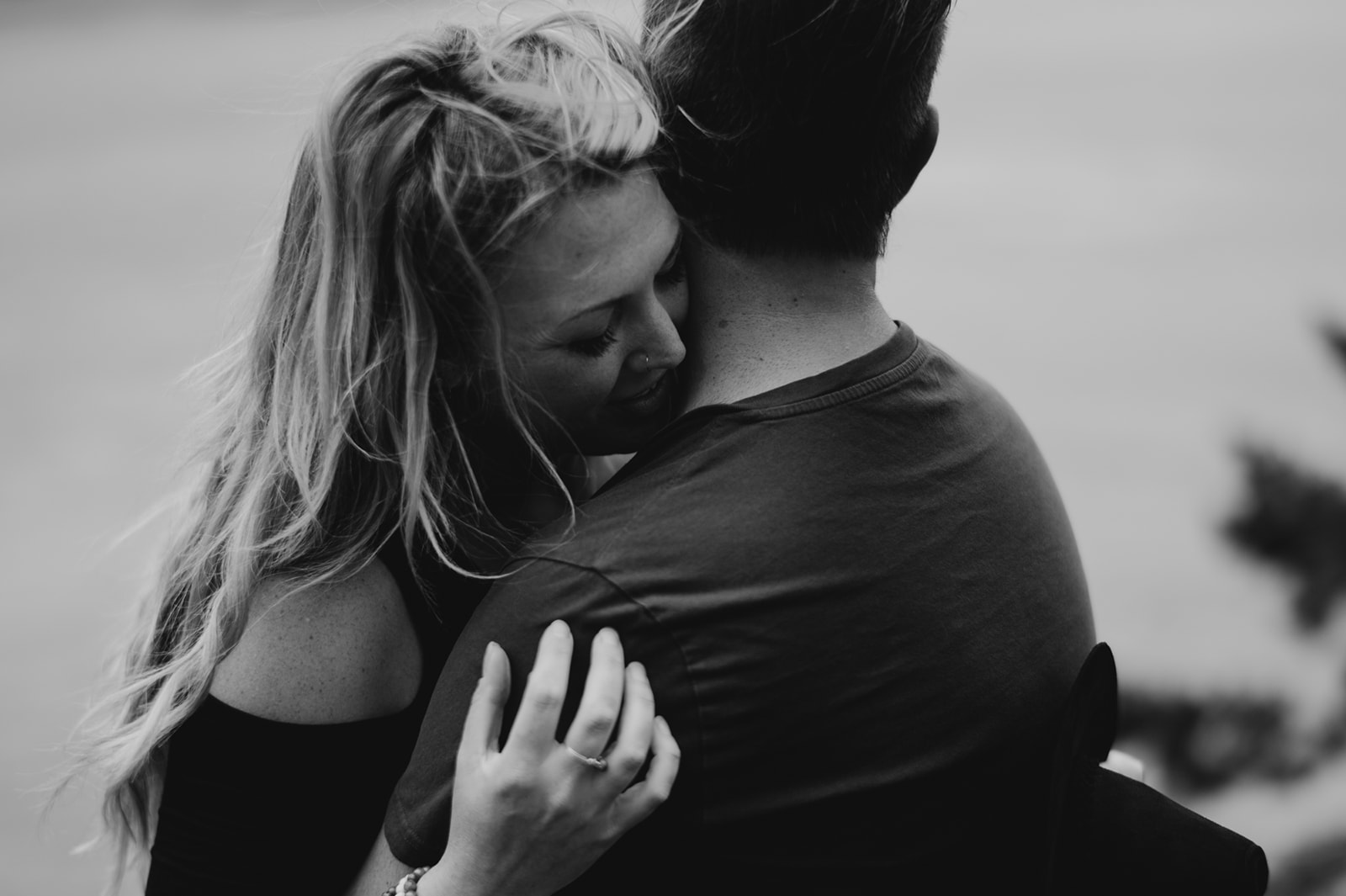 Couple embracing near a cliffside with a distant island in the background.