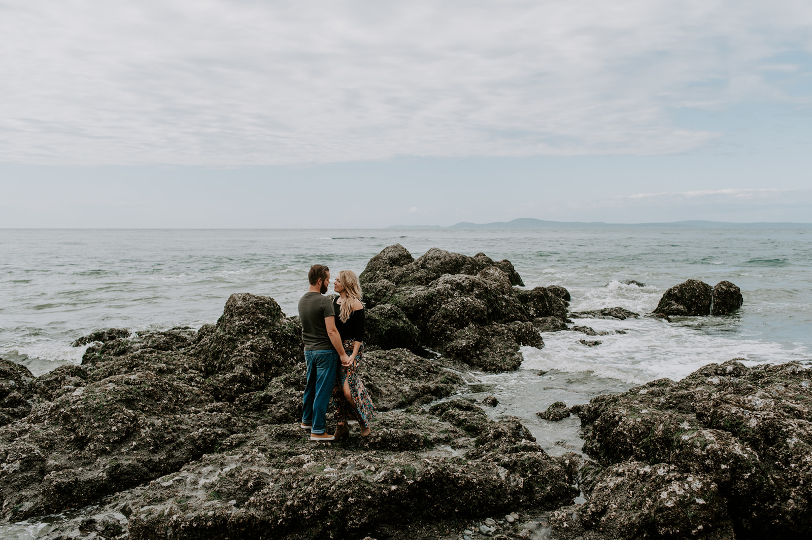 Couple standing on a rocky shoreline, gazing into each other’s eyes during their Deception Pass anniversary session.