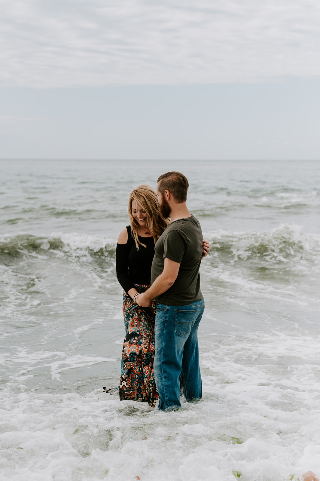 Couple holding hands in the ocean, sharing a tender moment as waves crash during their Deception Pass anniversary session.