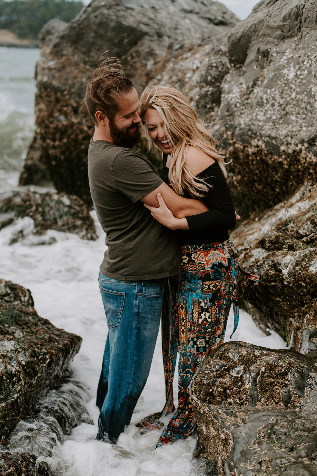 Couple laughing together as they embrace by the rocky shore during their Deception Pass anniversary session.