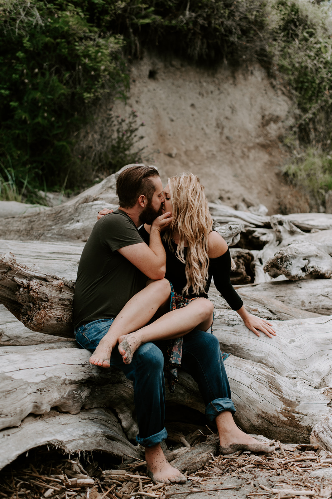 Couple sharing a passionate kiss while sitting on driftwood during their Deception Pass anniversary session.