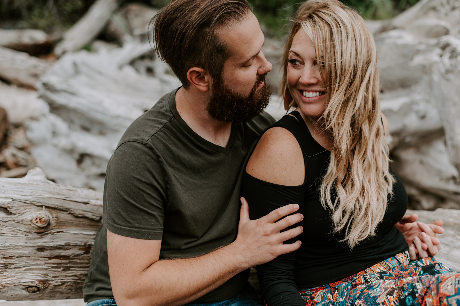 Couple sharing a sweet moment, sitting closely on driftwood during their Deception Pass anniversary session.