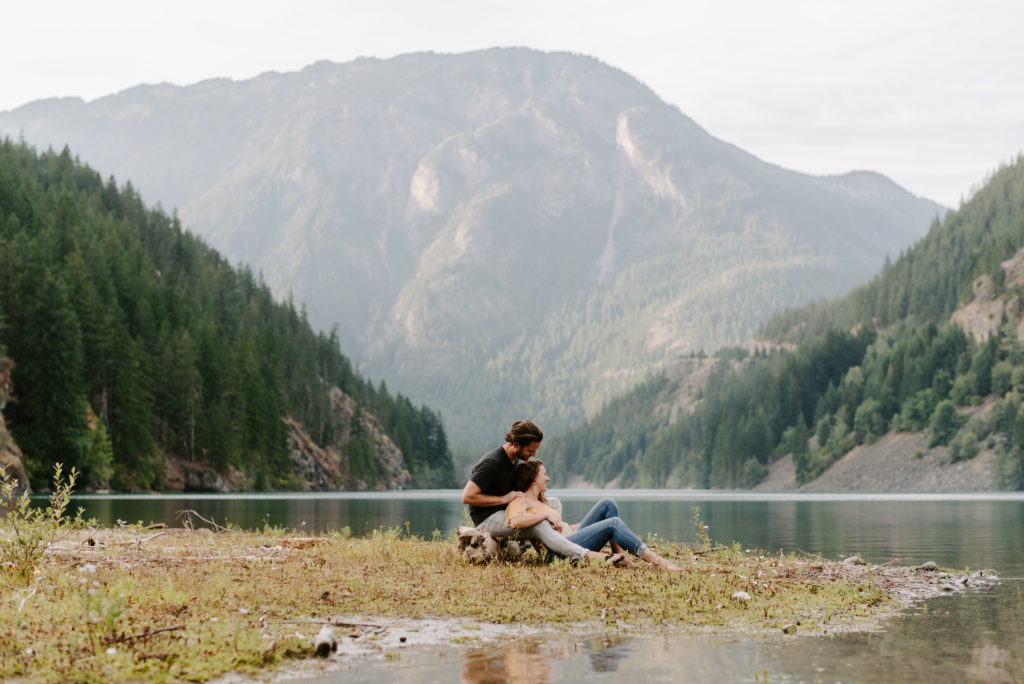 A couple relaxing by a mountain lake, surrounded by lush greenery and towering mountains.