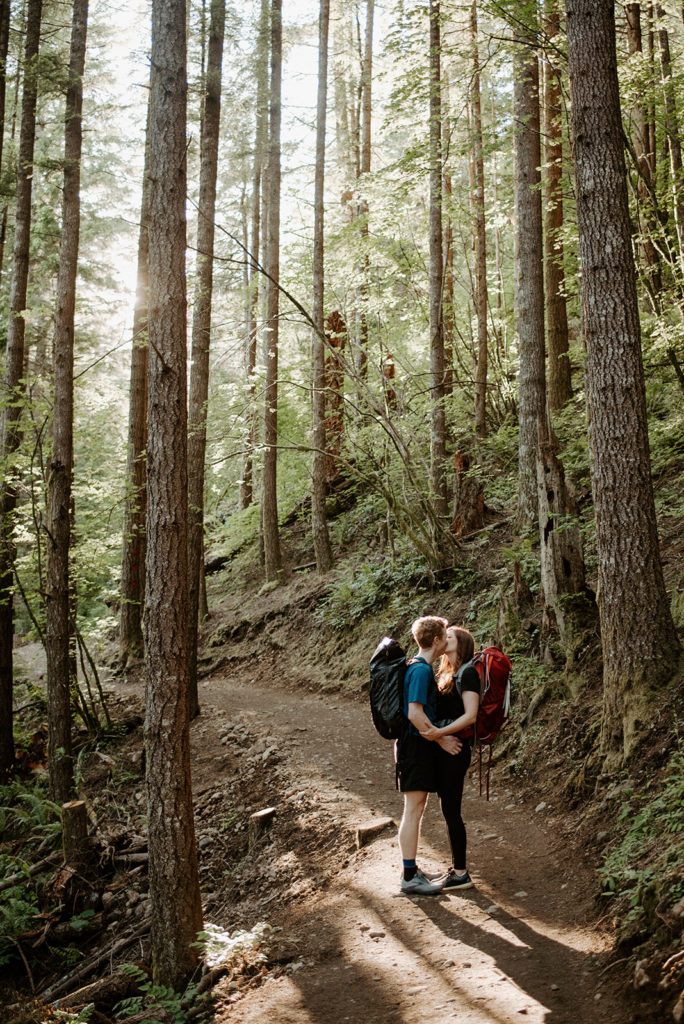 couple kissing in the forest, and long trees are around them