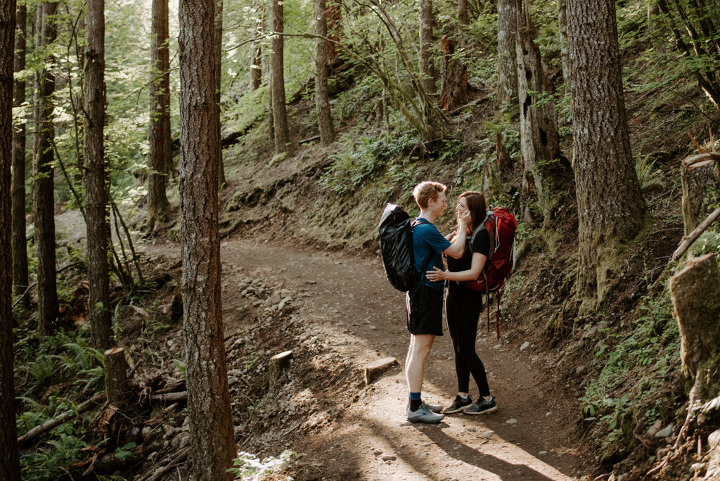 couple closely facing each other in the forest, and long trees are around them
