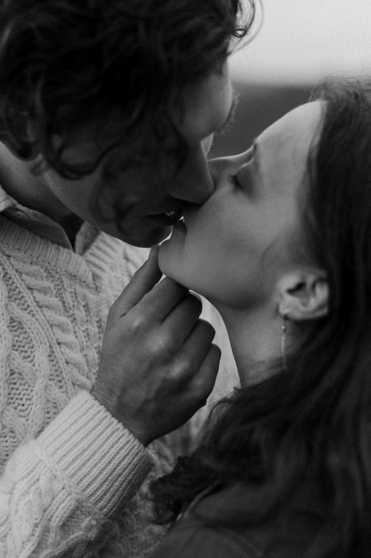A black and white close-up of a couple sharing an intimate kiss, with the man's hand gently touching the woman's chin.