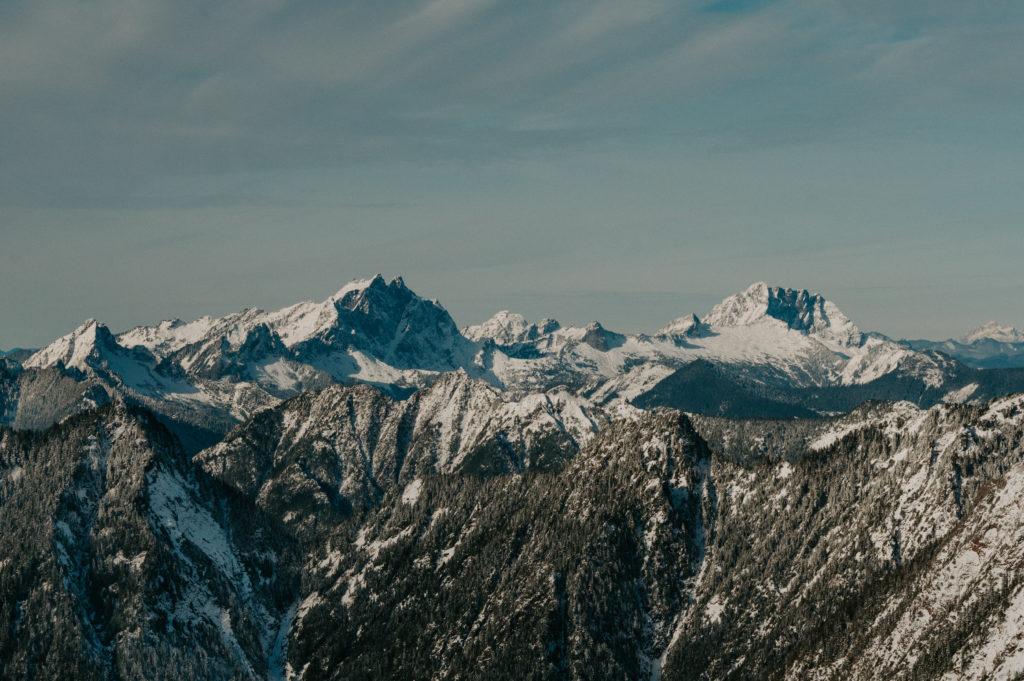 A panoramic view of snow-covered jagged peaks in the Cascade Mountains under a soft winter sky.