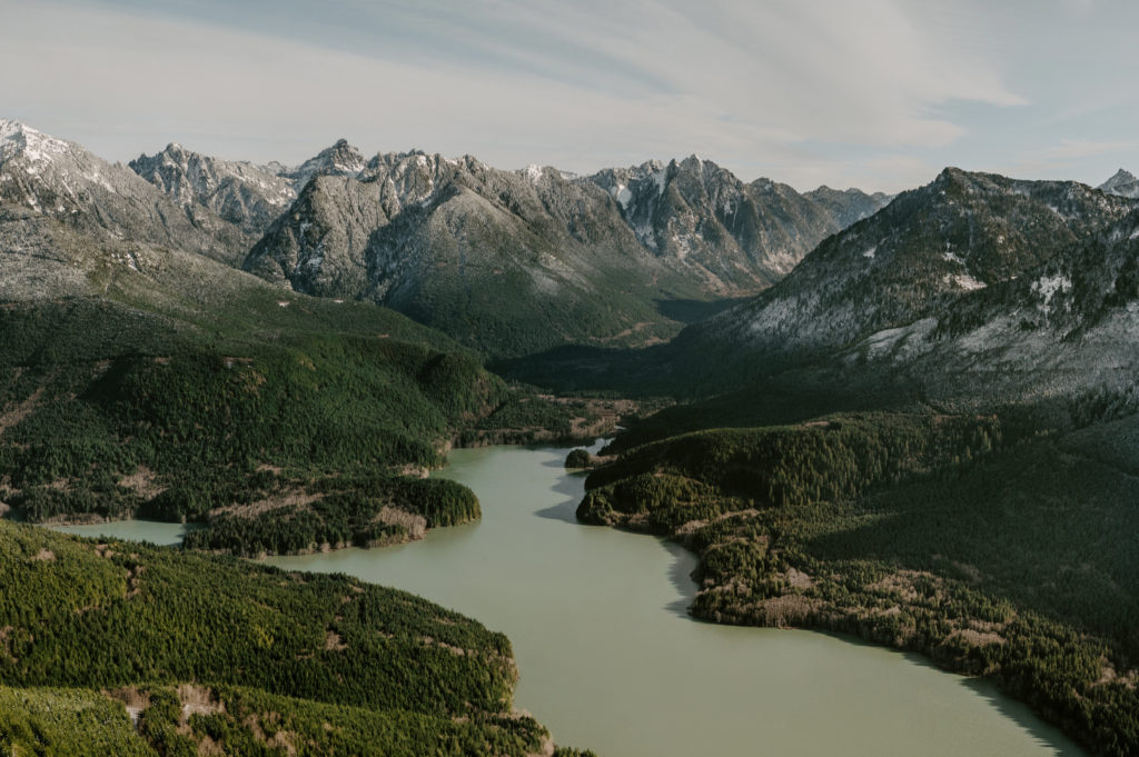 A winding river cutting through lush evergreen forests, with rugged mountain peaks in the Cascade Range.