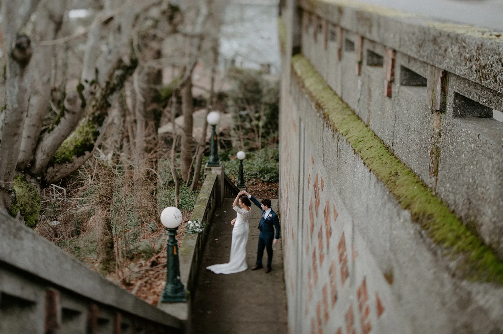 A bride and groom share their first dance on an outdoor pathway, surrounded by trees and vintage lampposts, creating a magical and intimate atmosphere.