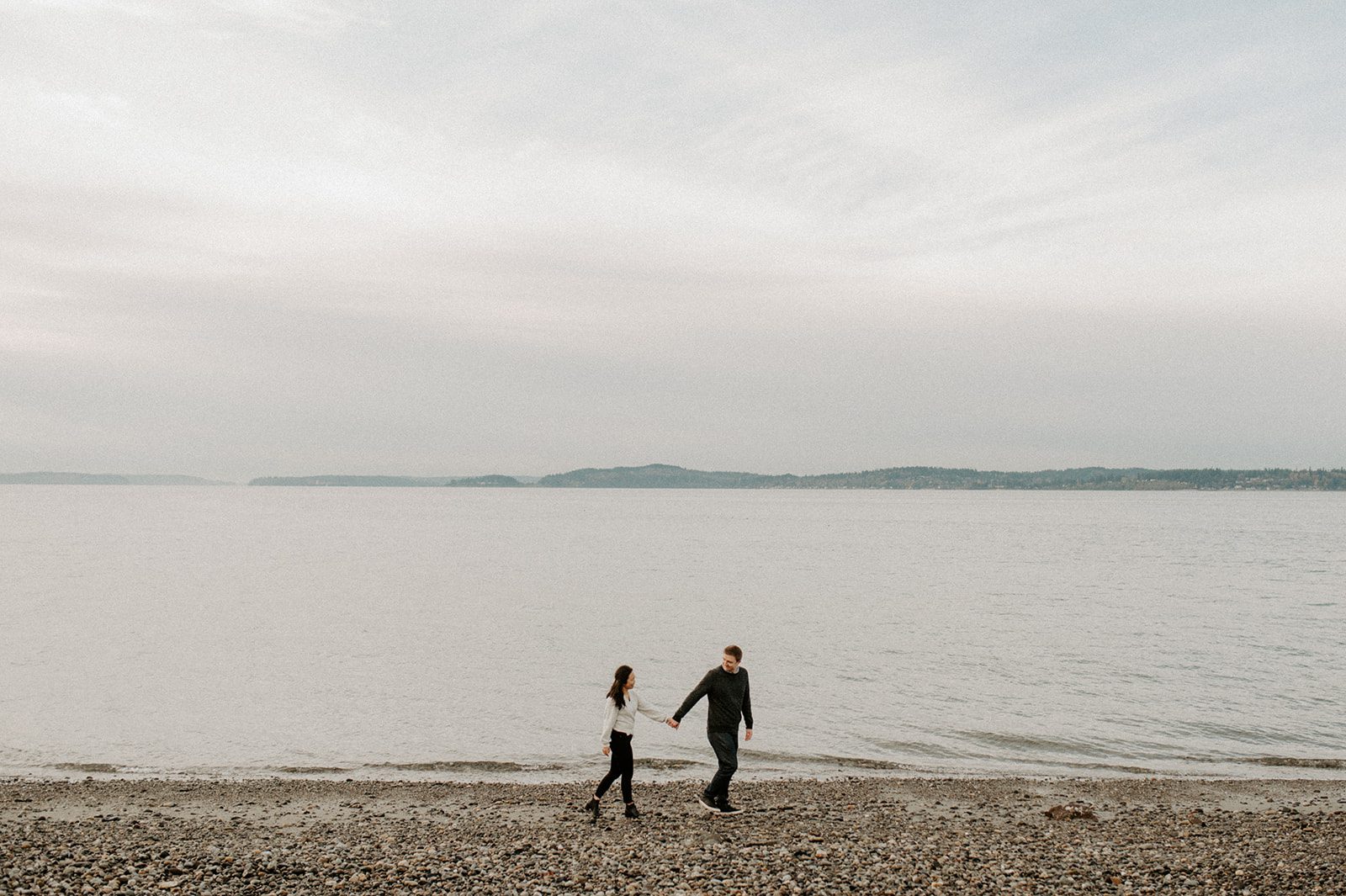 long shot of a newly engaged couple walking on a beach