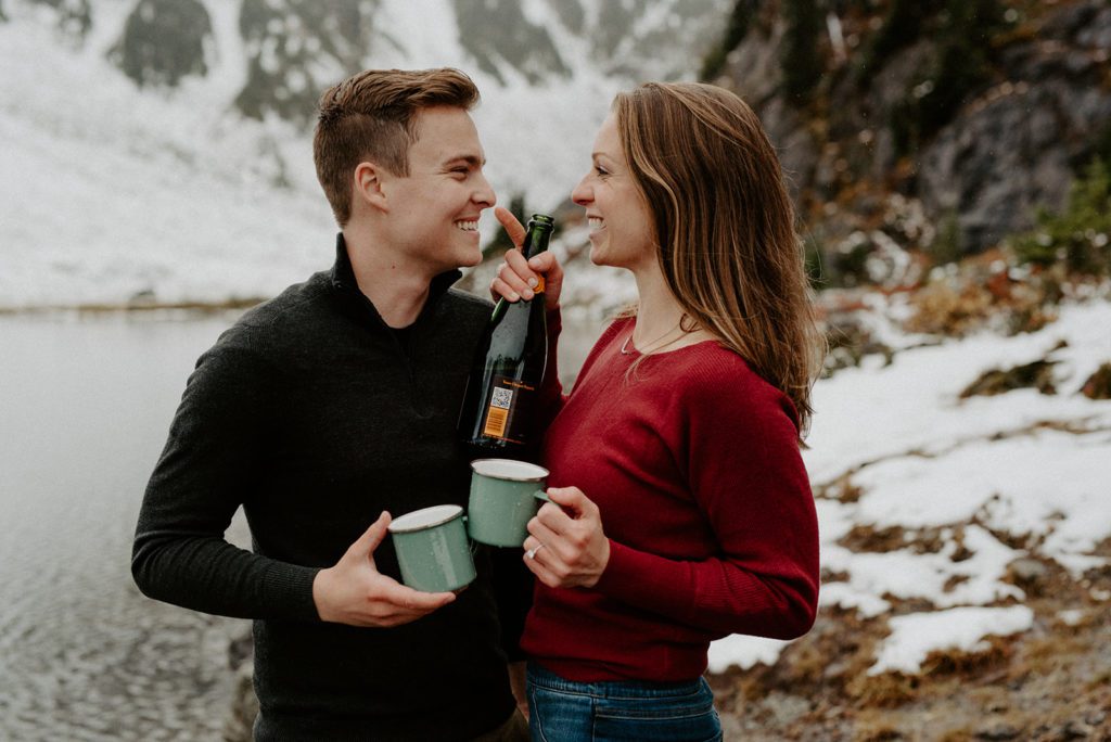 couple facing each other smiling big holding vine glasses on a mountain