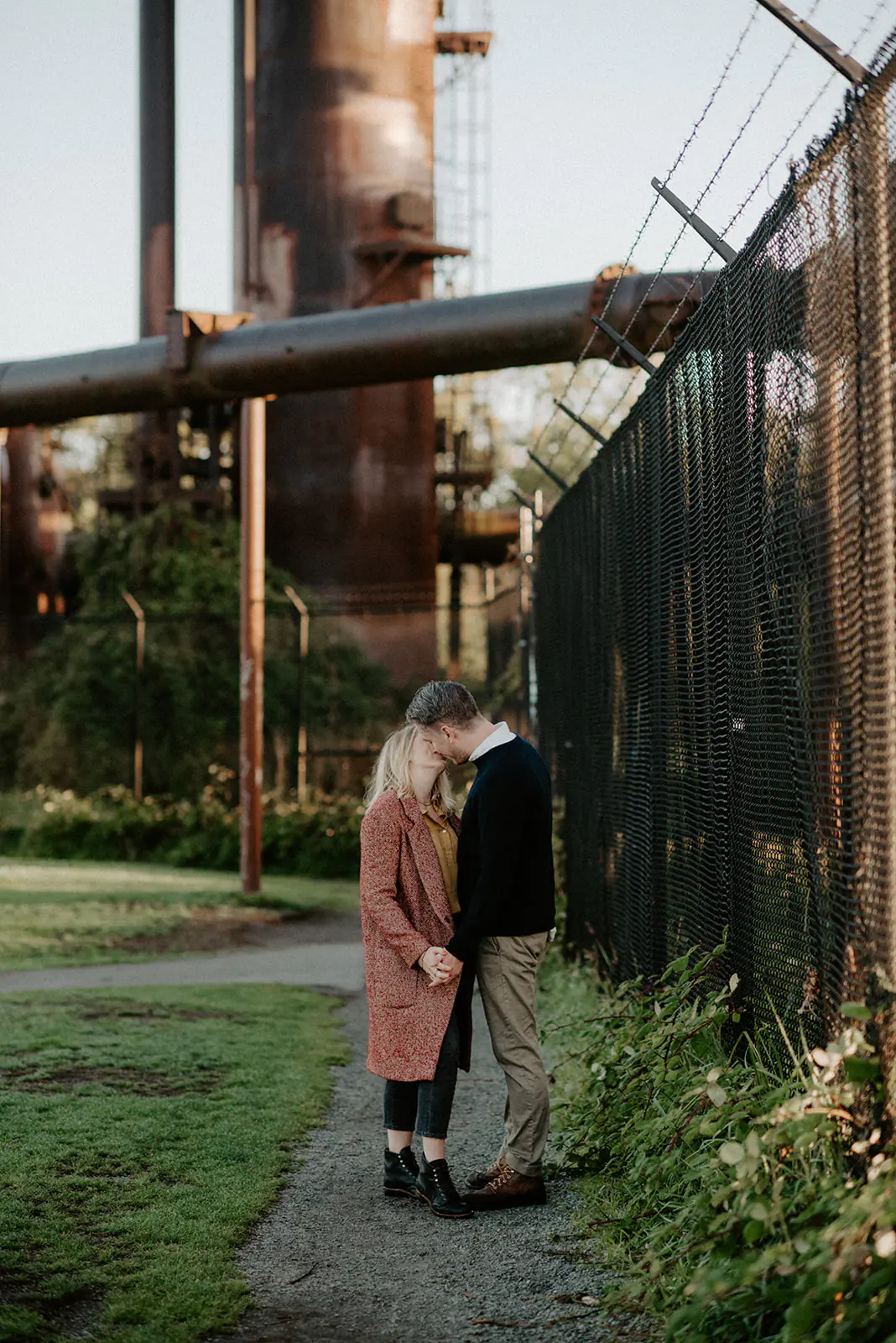 Couple embracing along a path with the historic gas plant in the background