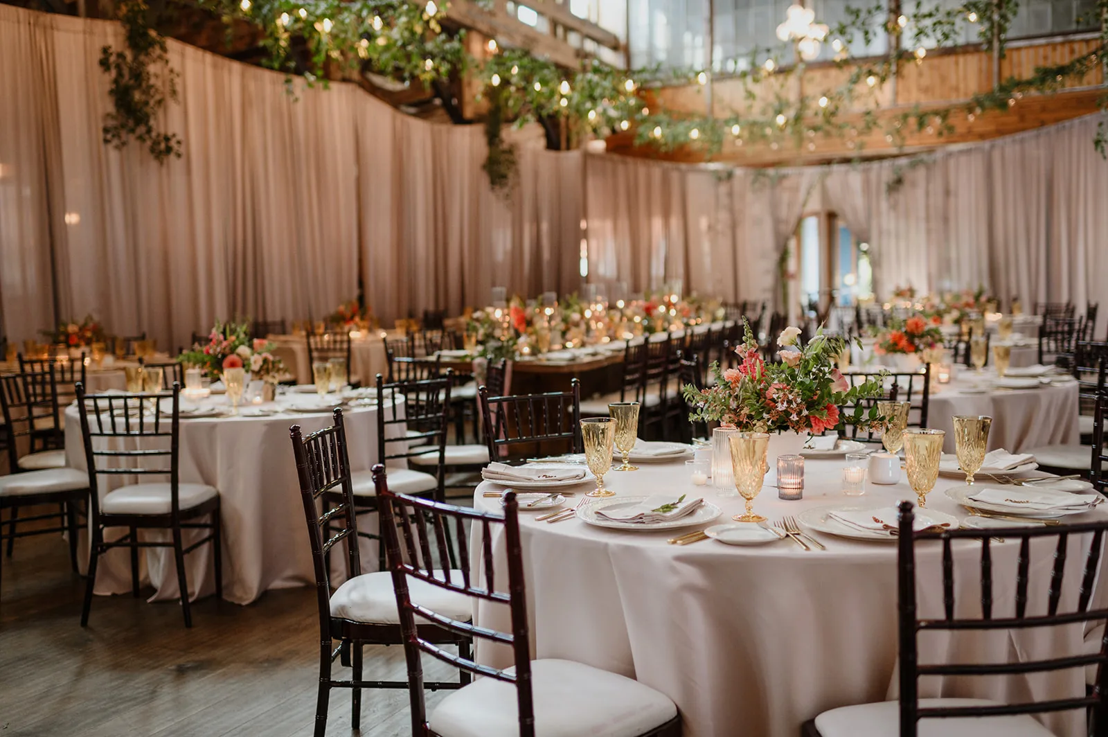 Elegant reception hall at SODO Park in Seattle, featuring round tables with floral centerpieces, string lights, and draped curtains creating a grand and sophisticated atmosphere.