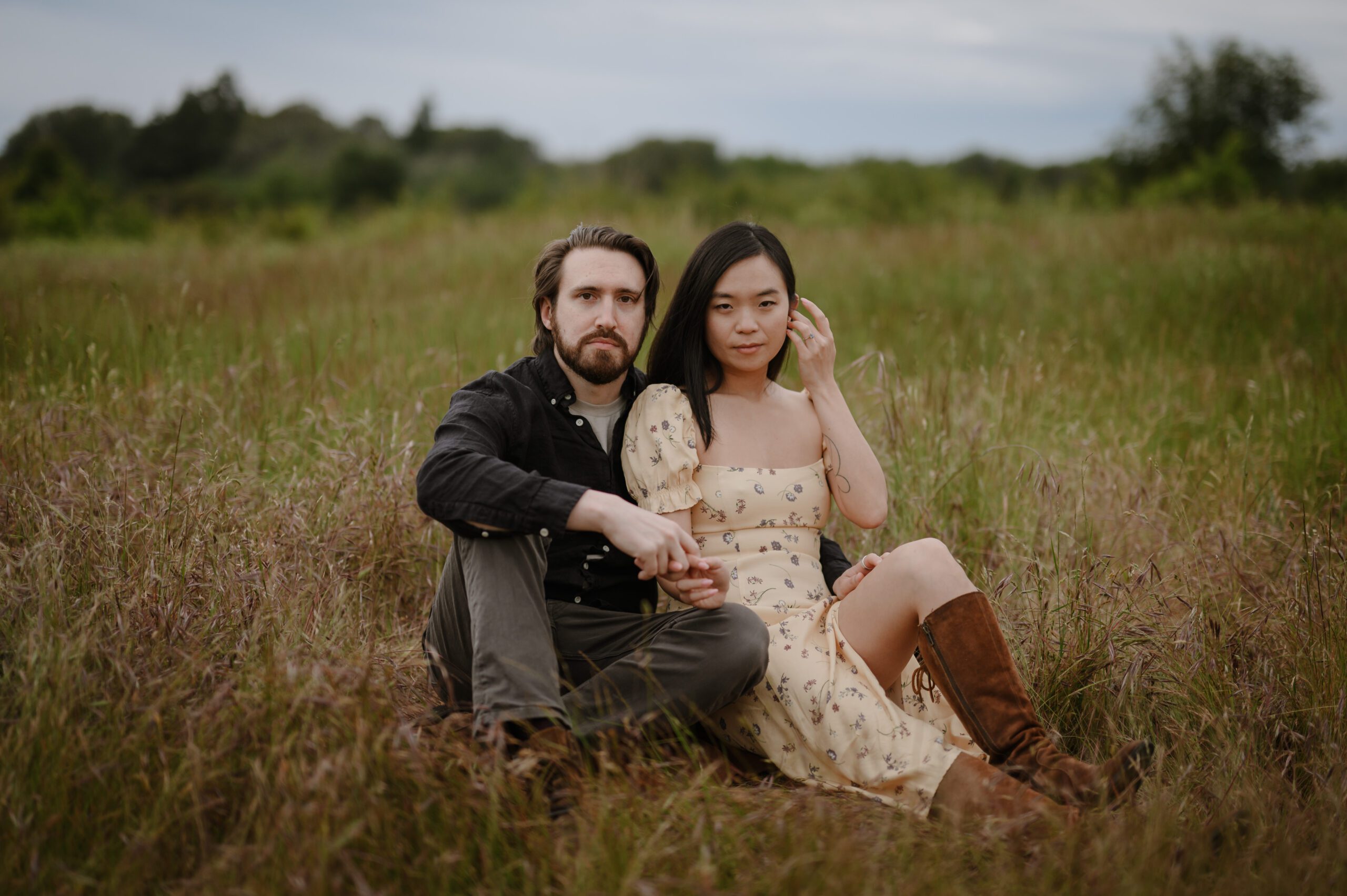 newly engaged couple sitting closely at a grassland area facing the camera