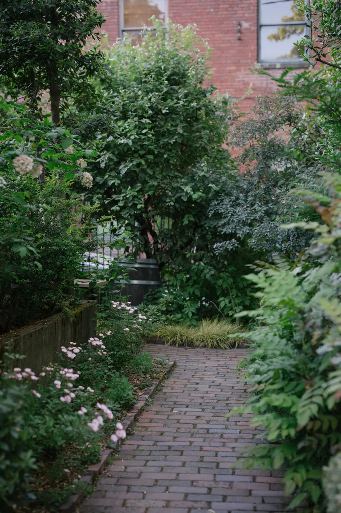 A serene brick pathway lined with delicate pink flowers and vibrant greenery leads to a peaceful garden area at The Corson Building, capturing the essence of Seattle's intimate wedding venues.