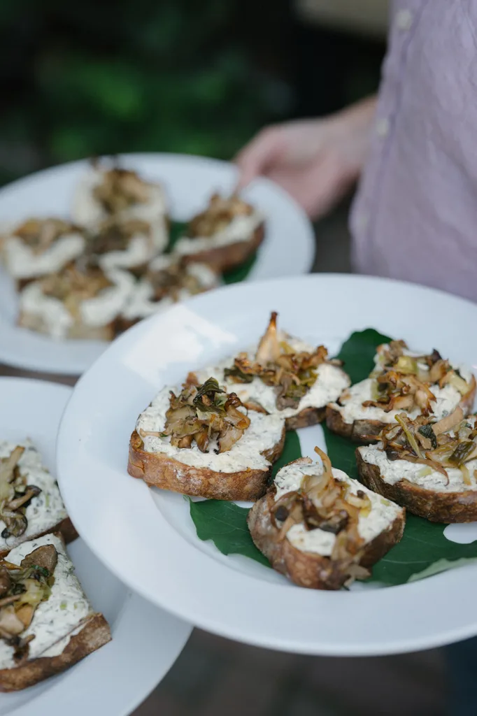 Waiter presenting a plate of artisanal toasts with creamy cheese and caramelized toppings, a sample of The Corson Building's exquisite wedding catering offerings in Seattle.