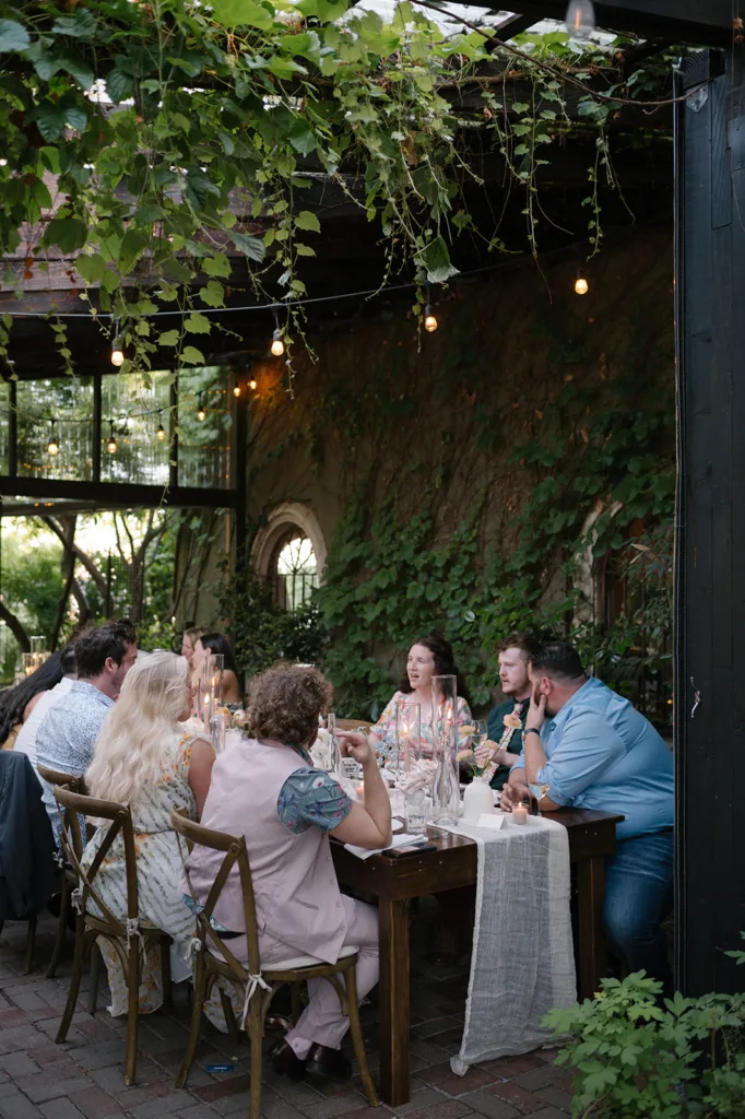 Guests enjoying a convivial wedding reception dinner at The Corson Building's outdoor space, adorned with natural greenery and soft lighting, epitomizing the intimate Seattle wedding experience.