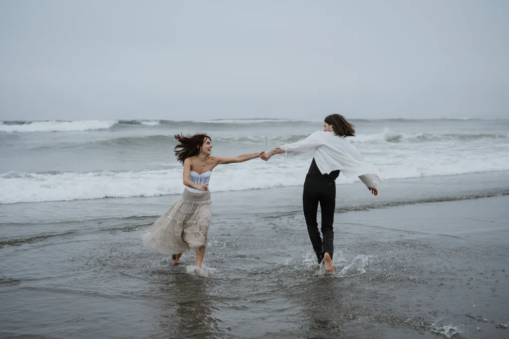 Engaged couple splashing in the ocean waves on a cloudy day