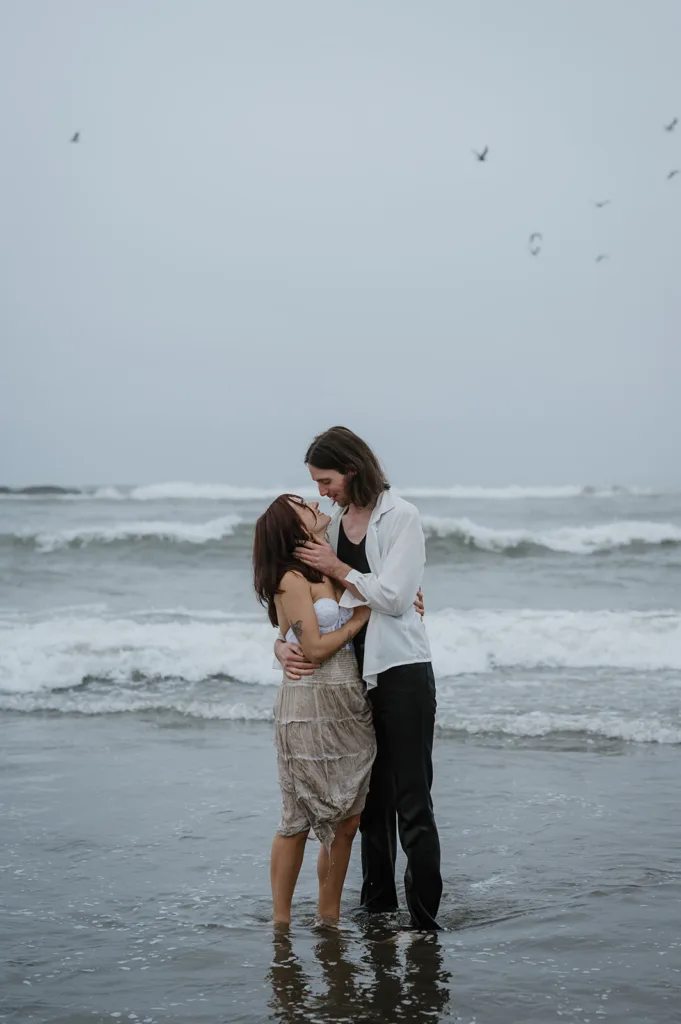 Couple sharing a tender moment amidst the ocean waves on a cloudy day