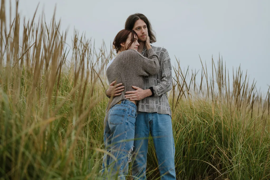 Couple hugging in tall grass on a cloudy day for Oregon coast engagement portraits