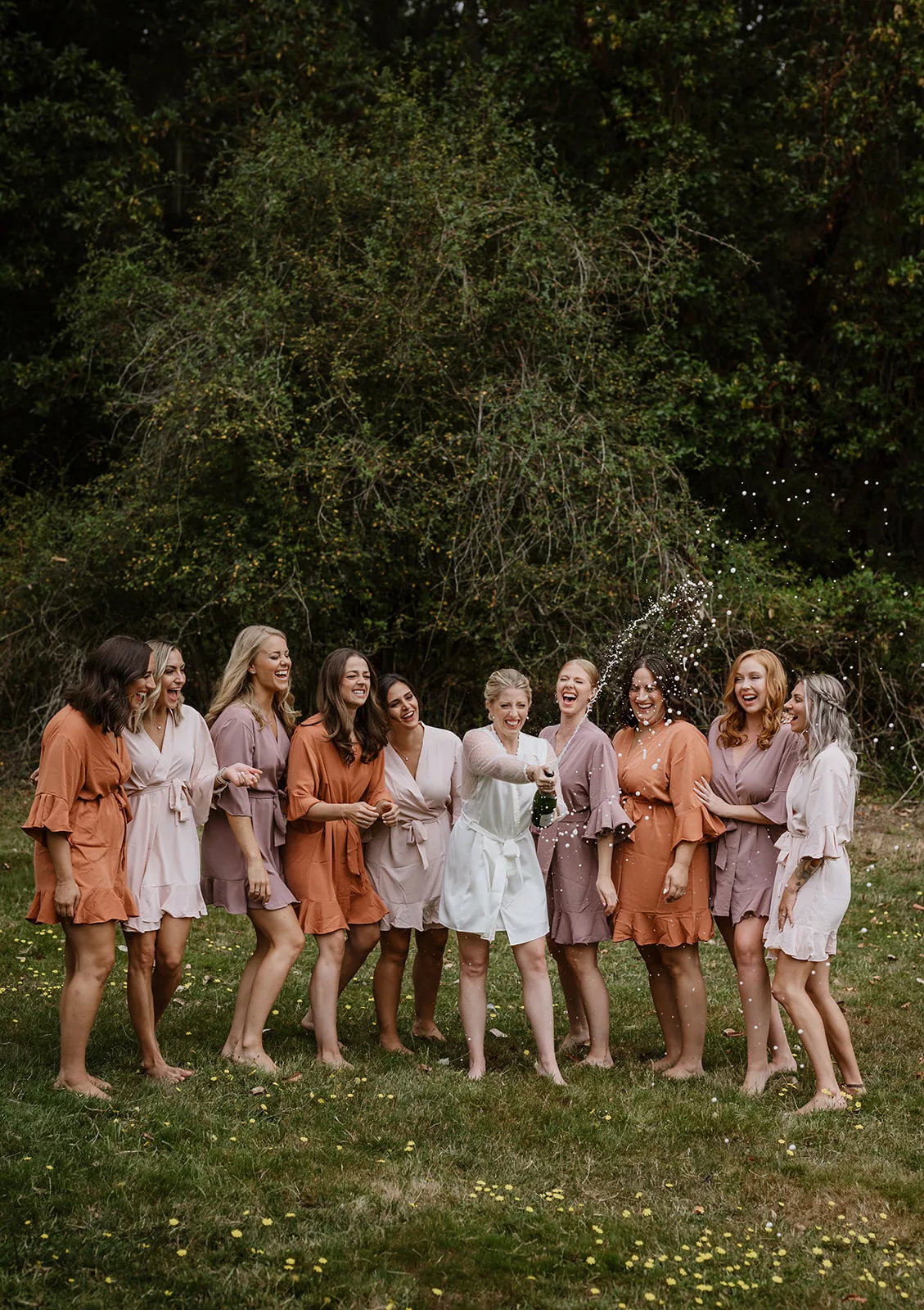 bride and bridesmaids in matching robes pop a bottle of champagne in celebration 