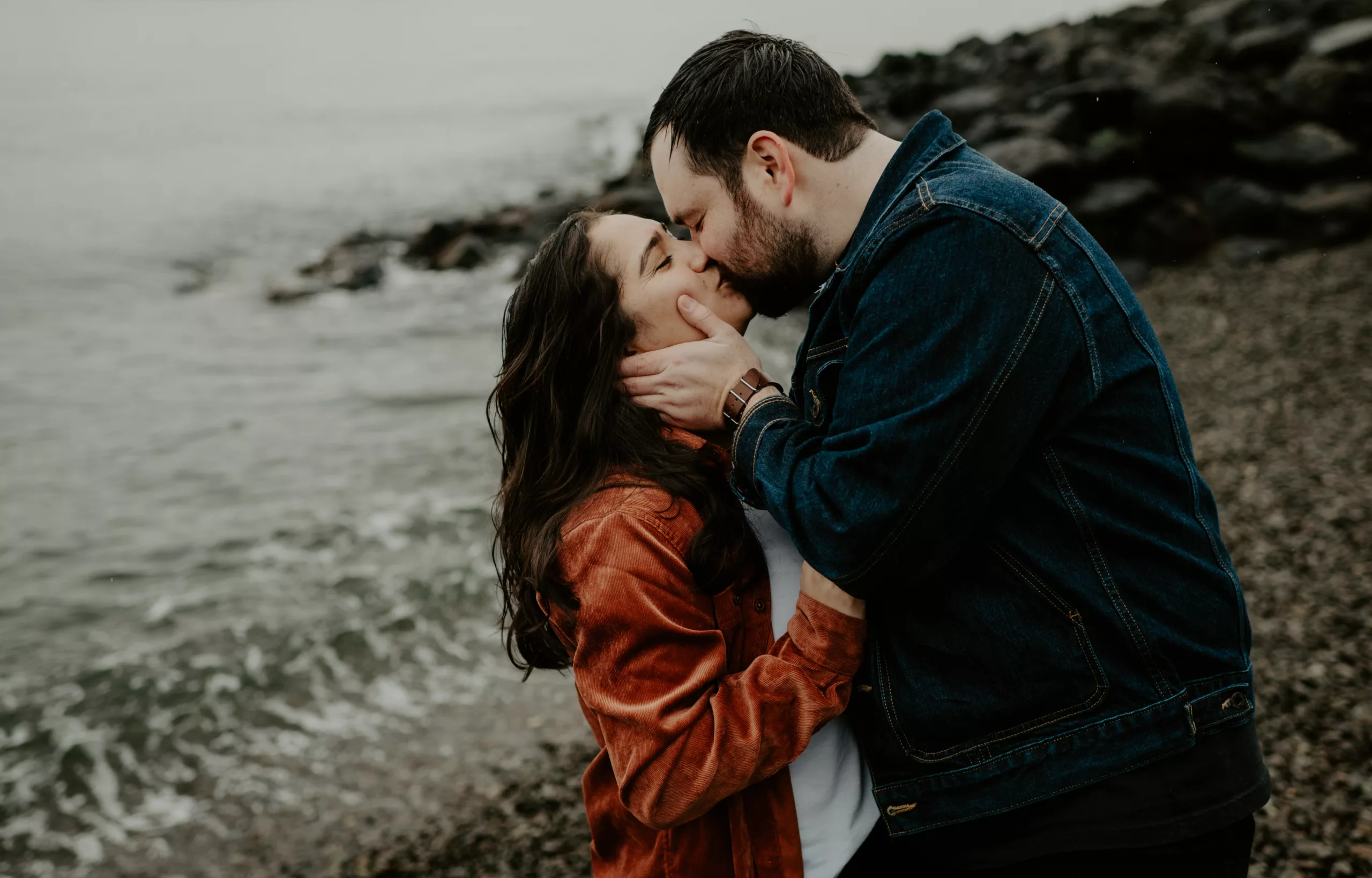 couple kisses on the beach during a rainy day