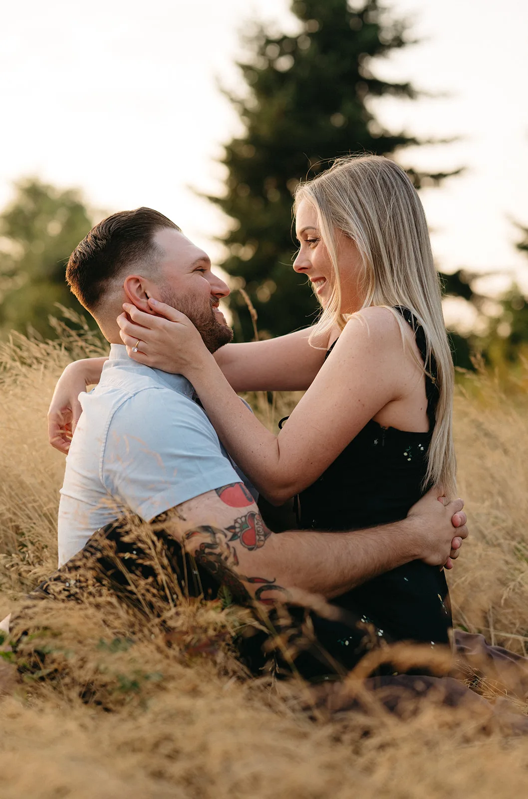 Couple embracing in a golden field at Discovery Park during sunset, smiling warmly at each other.