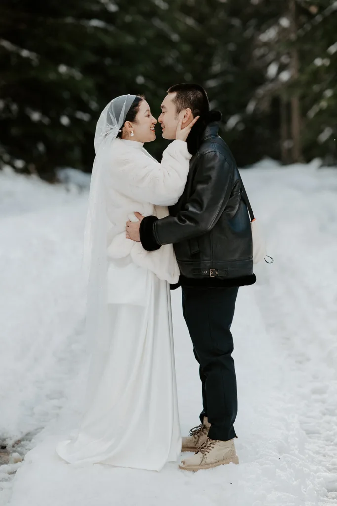 A candid moment of a bride and groom embracing each other, smiling joyously during their snowy mountain elopement, with the tranquility of the snow-covered trees around them.