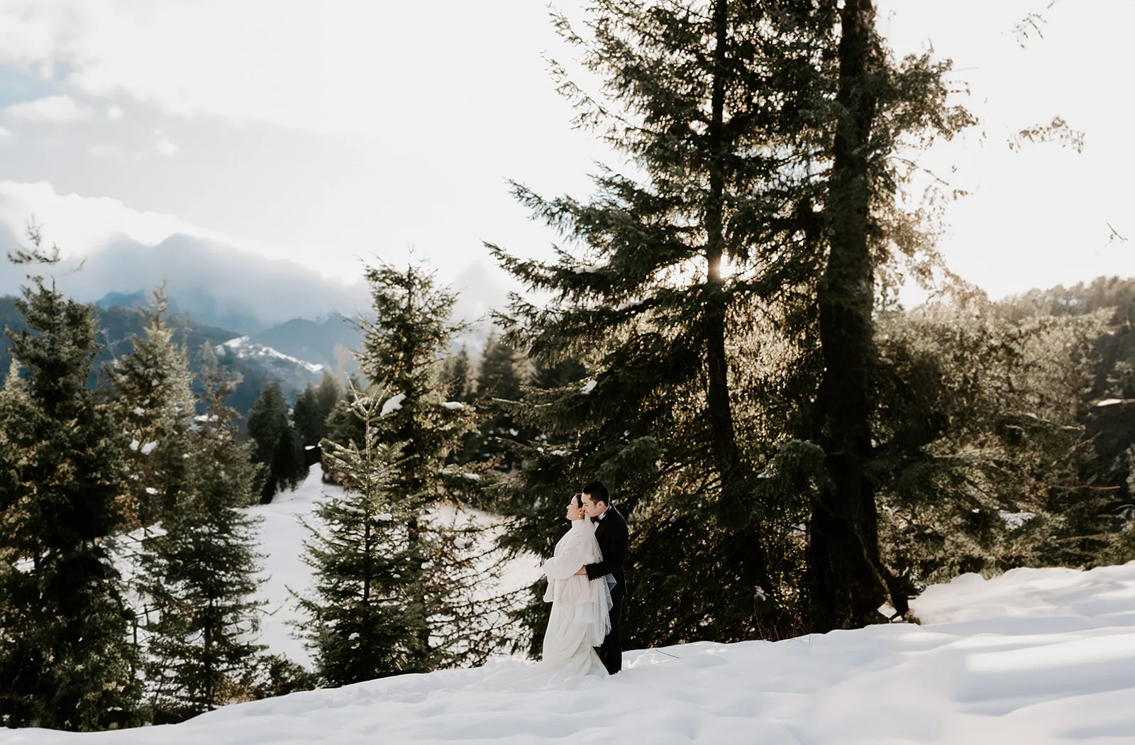 A couple shares an intimate cuddle in the snow-covered pine forest.