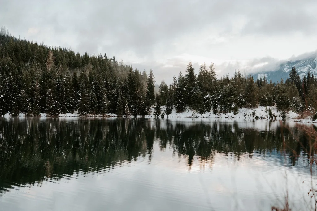 The serene waters of Gold Creek Pond reflect the snow-covered pines and mountains, offering a breathtaking natural backdrop for a peaceful and romantic winter elopement.