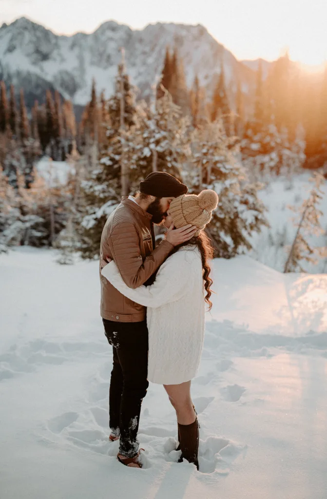 Couple kisses in the snow with a soft sunset behind the rugged peaks of Mount Rainier National Park.