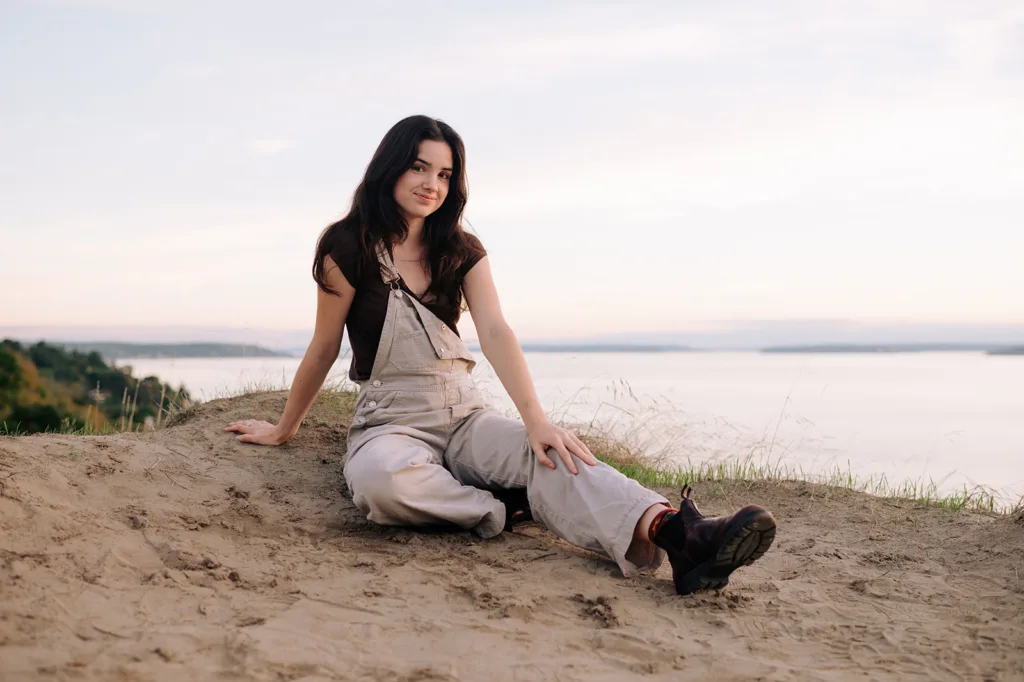 Young woman sitting on a sandy hill overlooking the water at sunset