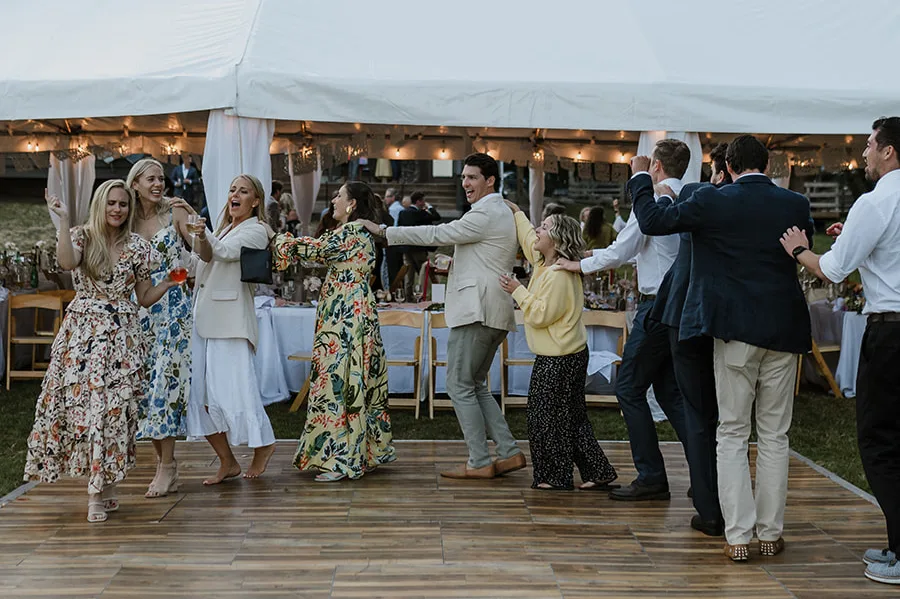 Guests happily engaged in a lively dance line at an outdoor wedding reception, exemplifying a fun-filled celebration under the twilight sky, a moment captured to inspire joyous wedding festivities.
