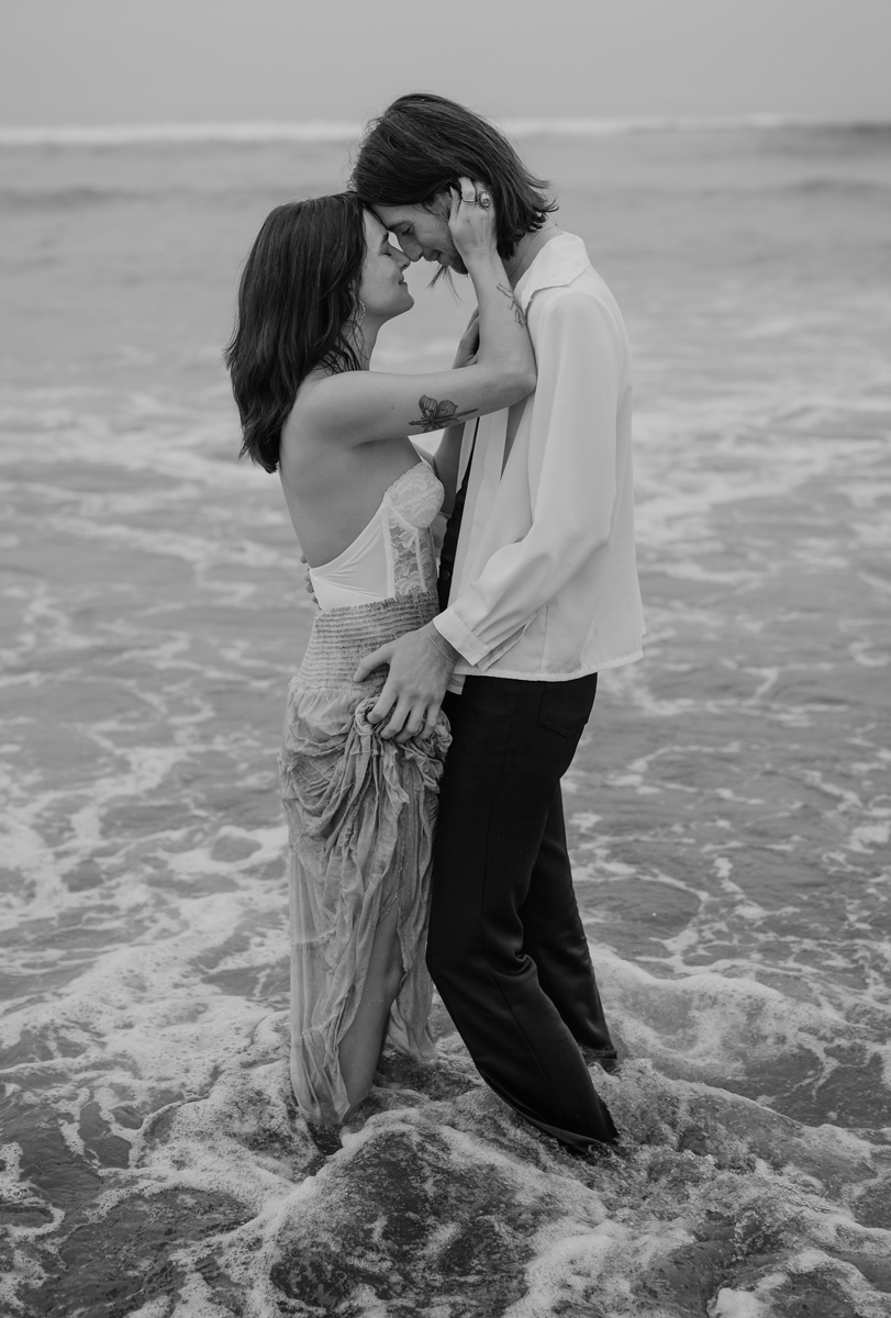 Black and white image of an engaged couple embracing in the ocean waves