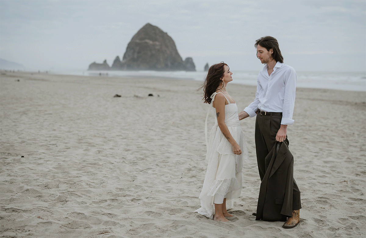 Couple holding hands on the beach with Haystack Rock in the background at the Oregon coast