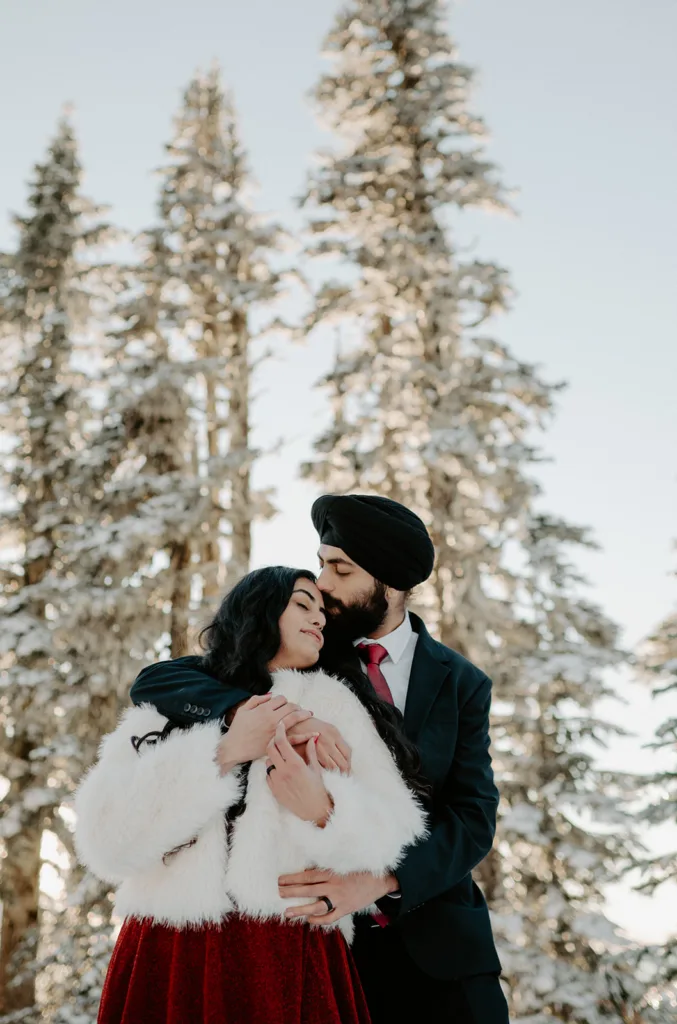 Engaged couple in a loving embrace with snowy pine trees in the background.