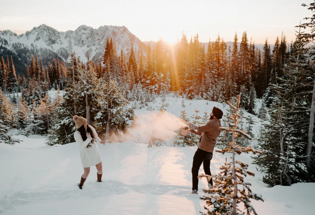 A couple playfully snow fights, with a golden sunset over Mount Rainier's forest.