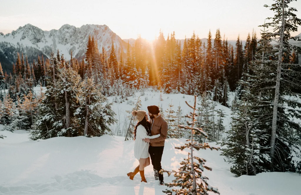 Couple stands in snow, facing each other, as sunset lights up Mount Rainier forest.