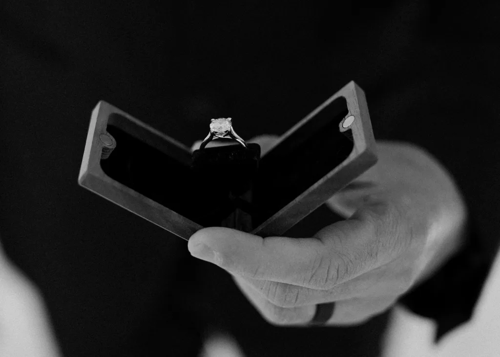 A hand holds an open engagement ring box, showcasing a sparkling diamond ring.