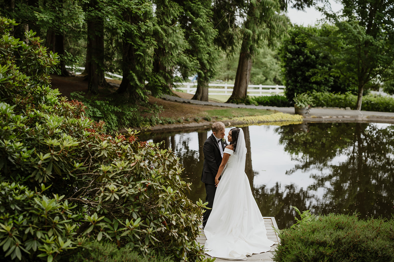 A bride and groom share a romantic moment by the tranquil pond surrounded by lush greenery at Chateau Lill in Woodinville.