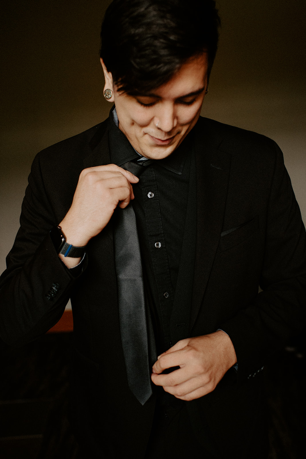 Groom in a black suit adjusting his tie while getting ready on his wedding day