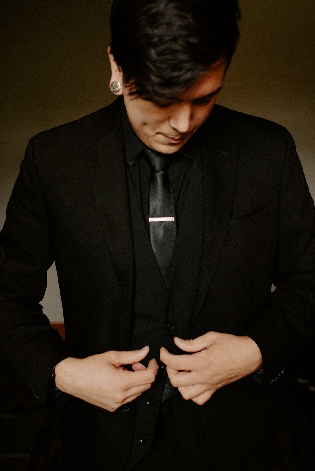 Groom in a black suit buttoning his jacket with a silver tie clip, getting ready for his Willows Lodge wedding