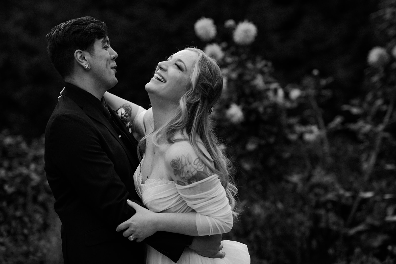 Black and white portrait of a bride laughing joyfully with her head thrown back as her groom holds her in the garden