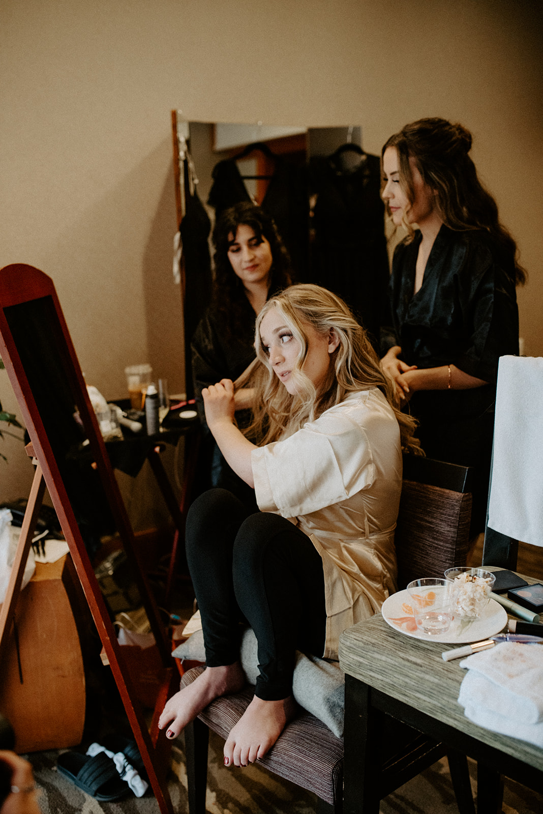Bride sitting and laughing while her hair is styled, captured candidly during getting-ready coverage