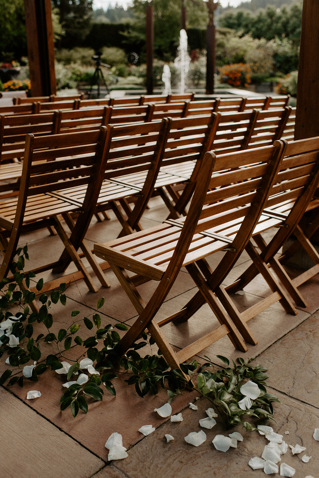 Wooden ceremony chairs set in rows with flower petals lining the aisle and a garden fountain in the background at Willows Lodge