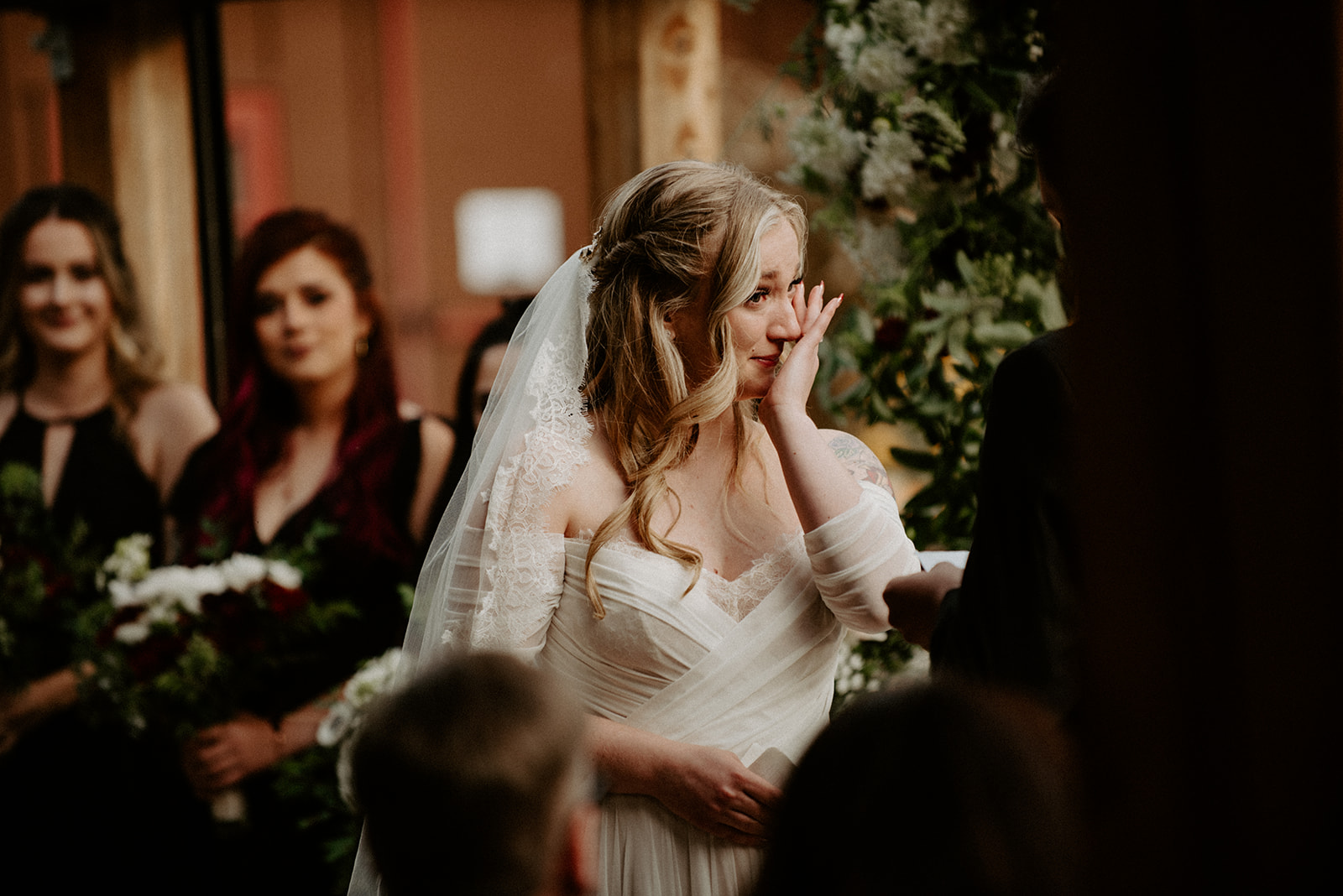 Close candid of a bride wiping happy tears during her wedding ceremony, her veil softly framing her face