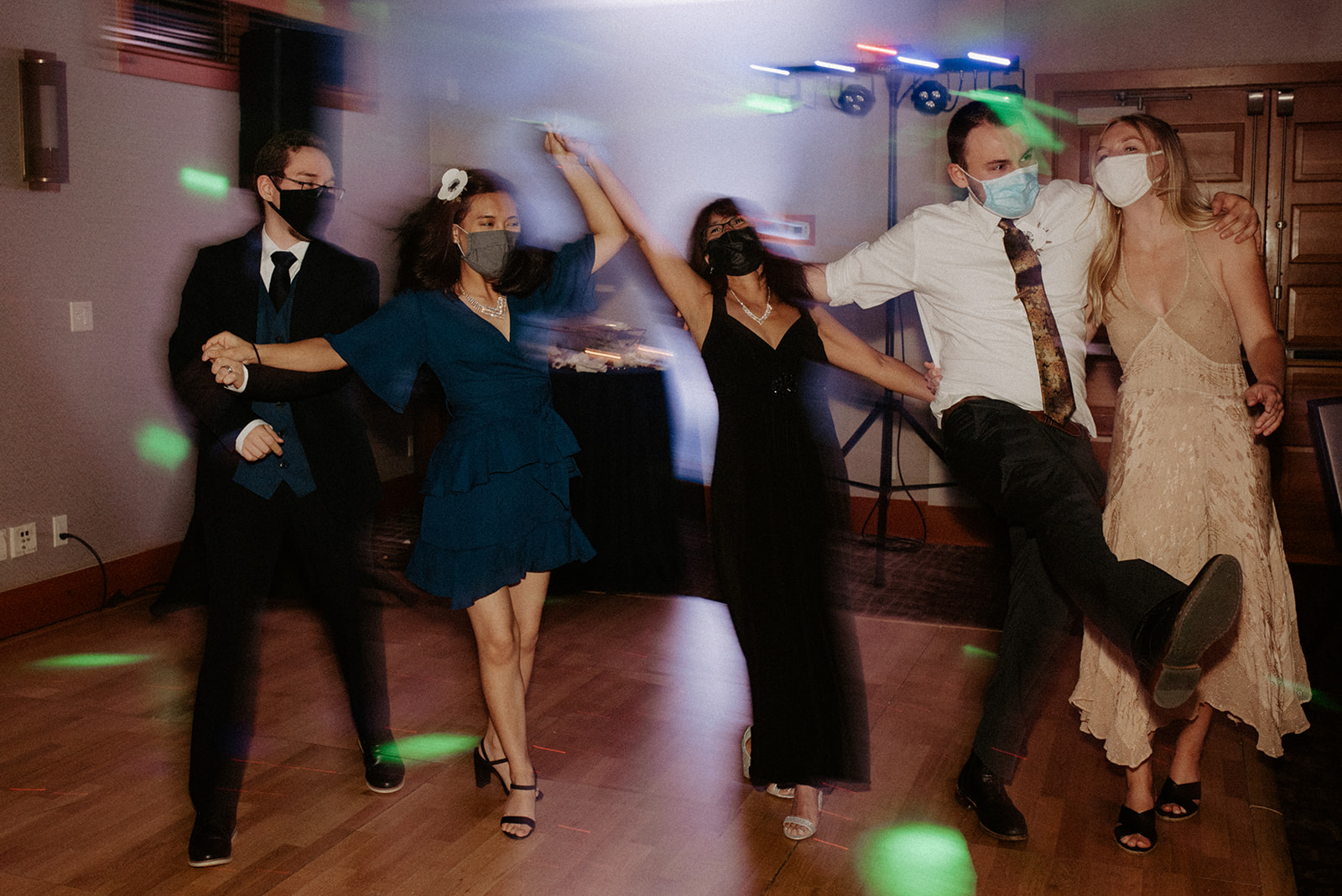 Guests dancing joyfully on the reception dance floor with colorful lights and motion blur capturing the energy of the evening